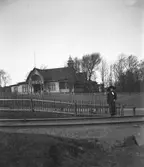 En ung kvinna står med ena foten på rälsen som ledde tågen söderut från Varberg före 1920. I bakgrunden ses Societetsrestaurangens gavel och spjälstaketen längs grusvägen däremellan.