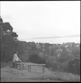 Kerstin Åsén sitter på Stadsparksberget i Jönköping, med Vättern i bakgrunden och stadsdelen Bäckalyckan nedanför.