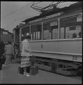 Kerstin Åsén vid spårvagn i Jönköping. Bilden tagen vid Torpaplan i Jönköping. Huset till vänster ligger på Klostergatan och det man ser genom spårvagnen ligger hörnet av samma gata och Erik Dahlbergsgatan.