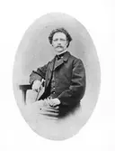 Sittande ateljéporträtt av skräddarmästare Jean Svensson i glasögon och med en käpp i ena handen.