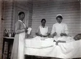 Sjuksyster med assistenter behandlar en ung paitent på Kustsanatoriet Apelviken i träpaviljongen. Till vänster står olika medikamenter samlade på ett litet bord.