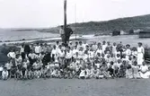 En stor samling skrofulösa (tuberkulos) barn som vårdades vid Kustsanatoriet Apelviken sommaren 1912. De minsta har burits ut med sängarna i det fria för att få sol, vilket var en del av behandlingen. Kanske är det samtliga som vistades där denna sommar. I bakgrunden syns stranden Lilla Apelviken med badhytter/bodar.