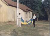 Staffan Bjerrhede och Berny Gustafsson hissar flaggan inför hembygdsgårdens midsommarfirande 1993. Hembygdsgården Långåker 1:3 ligger till vänster (ej i bild) och i bakgrunden ses Långåker 1:2 