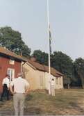 Staffan Bjerrhede halar ner flaggan efter midsommarfirande 1993. Berny Gustafsson och Gustaf Carlsson ser på. Till vänster ses den röda Hembygdsgården Långåker 1:3 och i bakgrunden Långåker 1:2 