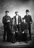Ateljéfoto av fem män med gevär och klädda för jakt. Mannen i mitten röker pipa. Gerhard Larsson beställde bilden.