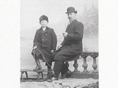 Snöbild. Ateljébild på man och pojke, där mannen sitter på en balustrad och pojken håller i en kälke som han satt foten på. Mannen till höger är John Ranch.