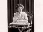 Kvinnoporträtt. Ung kvinna sitter med handen under hakan vid ett bord. (Se även bildnr MR2_1143)