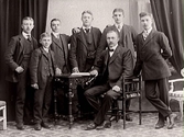 Sex ynglingar står vid en något äldre man, kanske en far med sina söner.