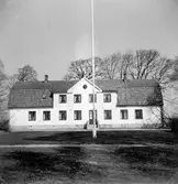 Exteriör av prästgården i Hasslöv. Byggnaden är putsad med frontespis med ett smalt gavelfält över mansardtakets övre takfall. En flaggstång är placerad i linje med den asymmetriskt placerade ingången.