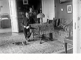 Interiör av salongen hos skohandlare David Larsson med fru Hilma Larsson. Framför dem ligger en katt på den orientaliska mattan.