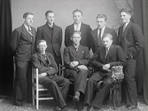 Ateljéporträtt av åtta unga män, beställt av John Carlsson som sannolikt även är med på bilden. Kanske är det en förening eller idrottsklubb.