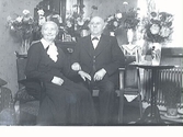 Herr och fru Andersson i sin bostad i kv Gamleby, Varberg, fotograferade med blomsteruppvaktning. Troligen firas guldbröllop.