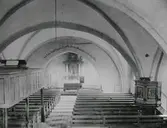 Kyrka i Våxtorps socken. Vy mot altaret i koret med ett svagt spetsigt korvalv. En läktare med mindre orgel står på pelare över bänkarna på norra sidan och predikstolen sitter utan tak på södra sidan.