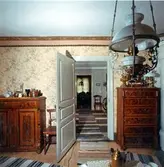 Interiör av hemmansägare Ivar Edins manbyggnad, uppförd 1852. Norra kammaren sedd mot SV. Skänk från 1909 snickrad av Axel Svanbom. Smörbytta inropad på auktion omkr 1905 efter Johanna Åberg. Stolen har tillhört H.Edin. Dragkistan snickrad av A. Svanholm omkr. 1910,  från mitten av 1800-talet. Tapeter och takbård från tiden omkr 1896.