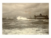 Havet i storm vid kallbadhuset i Varberg, sett från Barnens badstrand. Fartyg och, master syns bortom piren.