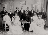 Konfirmationsgrupp med prästen i mitten omgiven av flickor i vida vita klänningar med puffärmar och gossarna uppställda baktill i kostym.