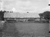 Ladugård med spåntak och framför den gödselstacken. En långsträckt kärra står tvärs över vägen fram till byggnaden.