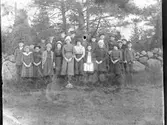 En grupp barn i olika åldrar står vid en stengärdsgård med barrskog bakom. Flickorna har tjocka mössor på sig men inga ytterkläder i övrigt. Ingen lärare finns med på bilden, så möjligen kan barngruppen höra till ett barn- eller sjukhem. (Bilden har svag dubbelexponering nedtill)