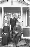 Familjebild med äldre makar på stolar vid farstubron och troligen sina tre barn stående bakom dem.