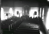 Interiörbild från Drängsereds kyrka vid en begravning. Fotot är taget från orgelläktaren mot koret. Vid kistan står män i höga hattar. Till vänster ses ett skrank som döljer trappan upp till predikstolen.