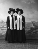 Ateljébild av två kvinnor klädda i ytterkläder. Båda damerna med hatt och halsduk. Beställare är Klara Bengtsson, Bönarp i Valinge.