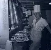 En kvinna vid färdiga maträtter. På kuvert som medföljde bilden står det: Stadshotellet Englund.