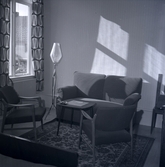 Stadshotellet inredning. Ett fönster, en golvlampa, ett par fåtöljer, en soffa och ett litet bord med askopp.