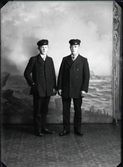 Ateljéfoto av två ynglingar i skärmmössor mot havsfond. Beställare: Gunnar Ljunggren.