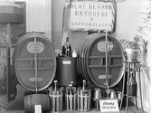 Olof Olssons bryggeri och kopparslageris monter på Hantverksutställningen i Gamlebyskolan, Varberg, 1927. Ölfat, tunnor, svagdricka i kaggar och kopparkärl visas upp i montern. Skylten påtalar att rökning där är förbjuden.