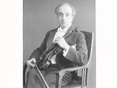 Kapellmästare Forgneri sitter med fiol och stråke i en karmstol. (Se bildnr GB2_3098-3101)