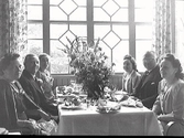Sex personer på middag på Societetshusets restaurang i Varberg. Någon firas sannolikt eftersom det står flera blombuketter på bordet. Trolig bildbeställare var Albert Nordström i Helsingborg, som även förmodas vara en av männen på bilden. (Se även bildnr GB2_3386)