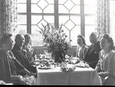 Sex personer på middag på Societetshusets restaurang i Varberg. Någon firas sannolikt eftersom det står flera blombuketter på bordet. Trolig bildbeställare var Albert Nordström i Helsingborg, som även förmodas vara en av männen på bilden. (Se även bildnr GB2_3386)