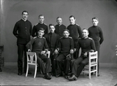 Gruppbild, unga män klädda i någon sorts uniform, men de är inte enhetligt klädda. De flesta bär en tröja med stora axelklaffar och ett runt emblem mitt på bröstet. (Ej tagen i ateljén på Torggatan)