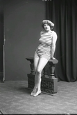 Ateljéfoto av kvinna i helfigur, iförd badräkt och badmössa. Hon står lutad mot en balustrad. (Se även bildnr GB2_4842)