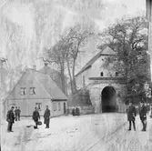 Gatubild vid Norre Port i Halmstad, sedd från Storgatan. Flera män i olika munderingar står längs vägen, vända mot fotografen. Den norra stadsporten ingick i det befästa Halmstad och stod klar 1601, alltså under danskt styre. Dess sneda vinkel gentemot Storgatan lär ha funktionen att förhindra beskjutning in mot staden. Varje natt stängdes alla stadsportarna till skydd åt invånarna. 

Stadsfullmäktige beslöt 1879 att riva portbyggnaden, men dåvarande riksantikvarien sa nej. Istället inrättade Hallands Museiförening (bildad 1886) där ett museum som öppnades 1899 och stängdes 1933. Norre Port blev byggnadsminne 2007.