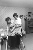 Hemtjänstpersonal hjälper boende till rullstolen, 1989