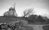 Väderkvarn med en stuga och uthus nedanför kullen, söder om Åskloster. I förgrunden en byväg och öppen grind i stengärdsgården.