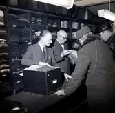 Grosshandlare Karl Danielsson bakom disken expedierar sina kunder tillsammans med Torsten Lundin dagen innan nyårsafton. Danielsson fyllde åttio år vid fototillfället.