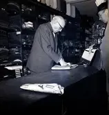 Grosshandlare Karl Danielsson bakom disken expedierar sina kunder tillsammans med Torsten Lundin dagen innan nyårsafton. Danielsson fyllde åttio år vid fototillfället.