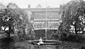 Mangårdsbyggnaden på Torstorps gård i Grimeton. Byggnaden har en står glasveranda i två våningar. Mitt framför den står en flaggstång vid en rund fontän, där en ung kvinna sitter på kanten.
