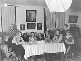 Fotograf Björkströms hem i kv Gästgivaren, där de bodde 1935-1937. Troligen har någon av döttrarna en bjudning då fotot visar nio unga kvinnor vid ett dukat bord. En kamera står i högra hörnet och i taket hänger blixtskärmen, så rummet fungerade sannolikt även som ateljé. Fotografierna på väggen föreställer: överst lotsen Halldén, under till vänster Märta Björkström som barn, i mitten Folkskollärare Nilssons barn och till höger rektor de Vylder vid Katrinebergs folkhögskola. Fotografierna fungerade som en slags reklam för fotoverksamheten. De hemmagjorda blixtarna som syns i taket bestod av 5 st 1000 watts lampor.
(Se även bildnr GB2_4138.)

I huset hade tidigare funnits kafé Mignons bageri och apotekets laboratorium. Ateljén hade tidigare funnits i hörnhuset vid Torggatan-Östra långgatan men man flyttade 1933 till kv Gästgivaren och 1937 tillbaka till kv Apotekaren i gamla Apotekets lokaler.