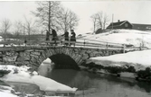 Gammal murad landsvägsbro vid Hjälmared i vinterskrud. Fyra personer passerar, varav en med cykel, på bron.