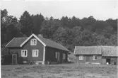Gård söder om Anneberg, Tölö. Bostadshus och uthus med skogsklädd höjd bakom.