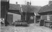 Stensatt innergård i Kungsbacka med bostadshus och andra byggnader. Mitt i bild ligger flera tunnor och till höger står en dragkärra.