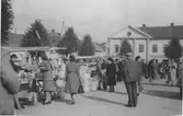 Marknadsbesökare på Kungsbacka torg år 1948 där bland annat laggkärl ocholika slags korgar saluförs. Bussar står parkerade på torget, men kring denna tid flyttades bussparkeringen till järnvägsstationen. 

I bakgrunden ses byggnaden i kv Tullen 8, kallad Gamla Gästis eller Medinska fastigheten, som var en av de första byggnaderna som uppfördes efter den stora branden i Kungsbacka 1846. Då var den ett av få tvåvåningshus i staden. Vid tiden för bilden låg Göteborgs Bank och en Möbleringsbolaget i huset. Den 16 september 2006 ödelades det anrika huset i en ny brand.