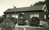 Bostadshuset på Välås nr 5 i Vallda socken. Framför huset står flera figurklippta buskar och till höger står flera mjölkkannor på tork.