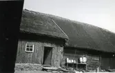 Gammal ladugård med halmtak och mjölkkannor på tork längs väggen av skiftesverk. Kockagården, Källstorp 3:7 i Värö.