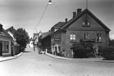 Östertullgatan i Laholm kantad av affärsbyggnader; närmast i bild till höger en modebutik, Lilla hembageriet och värdshuset Göta. Några människor står utanför bageriet. I skyltfönstret till vänster står det 