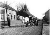 Flera vuxna samt hästdragen vagn på Storgatan, med S:t Laurentii kyrkan i bakgrunden