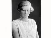 Ateljéporträtt av en ung Astrid Andersson, Tjärby Grimeton. hon bär en armlös klänning och ett långt pärlhalsband med knut på.